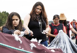 Chenoa McCarthy (left) spreads feathers over the totem pole before it was raised, in Opitsaht, on Meares Island, on July 1, 2022.