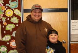 Kevin Jules stands with his son Noah under a picture of his graduating class from 2000.