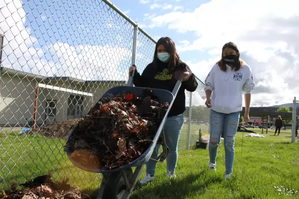 Sisters Daisy and Denise John cart leaves over to the site of the school's new garden.