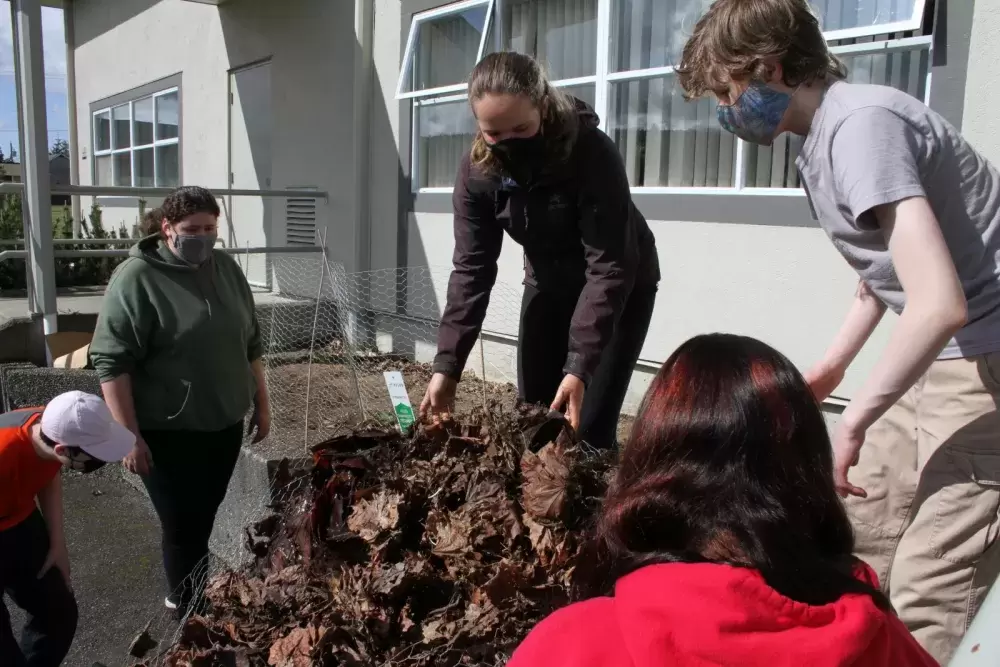 Gabriella Stanley (centre) Gracie Martinez (left), Julian Larrivee-Woods and other students in the Grade 8-9 class move leaves that have been composting by the Eighth Avenue Learning Centre over the winter.