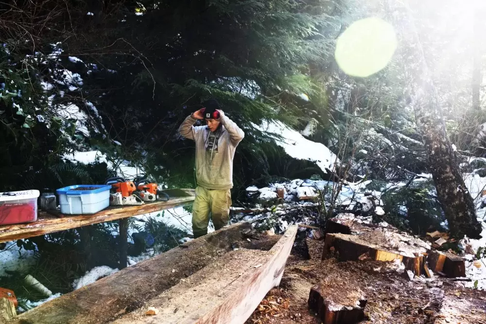 Ryan Sabbas helps Joe Martin carve a canoe for Valeen Jules within Tla-o-qui-aht First Nation traditional territory off the Pacific Rim Highway, on Feb. 16, 2021. 