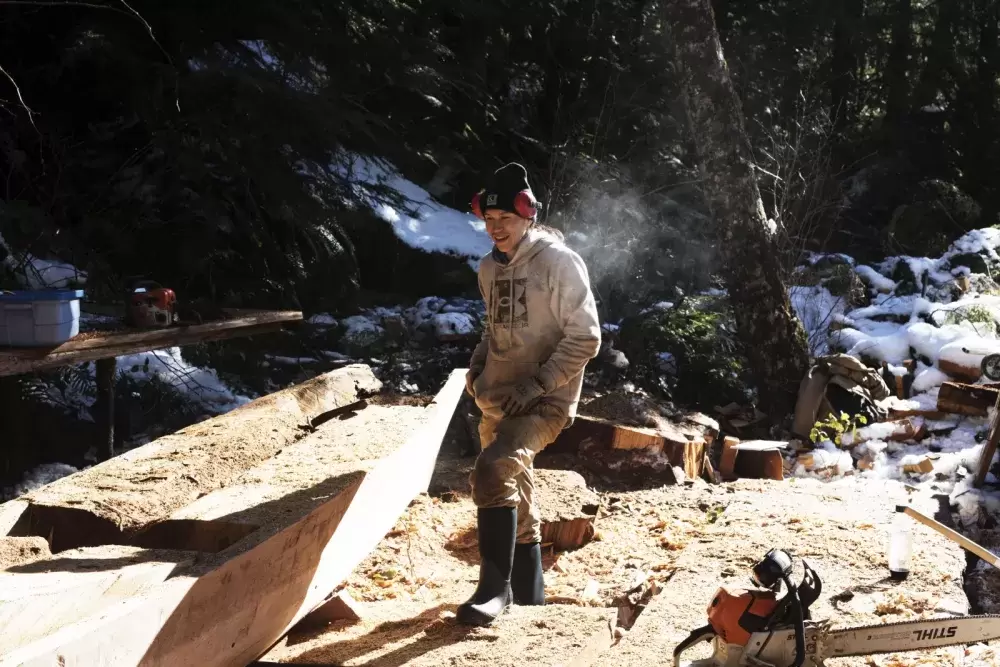 Ryan Sabbas helps Joe Martin carve a canoe for Valeen Jules within Tla-o-qui-aht First Nation traditional territory off the Pacific Rim Highway, on Feb. 16, 2021. 