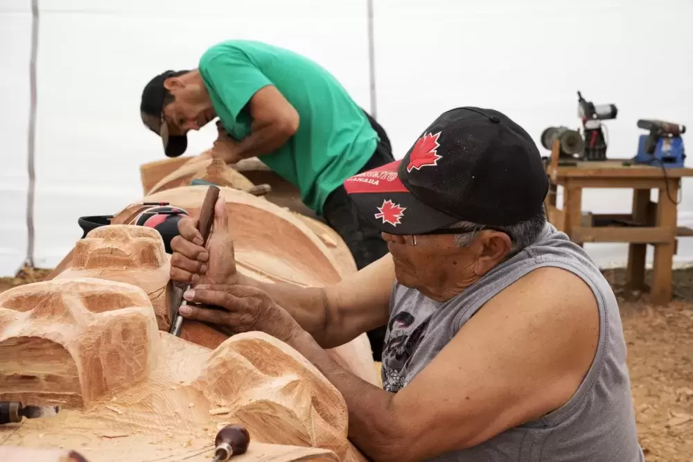 Robin Rorick (left) and Robert Martin (Nookmis) carve a totem pole inside a tent set up at the Tofino Botanical Gardens, on July 9, 2021.