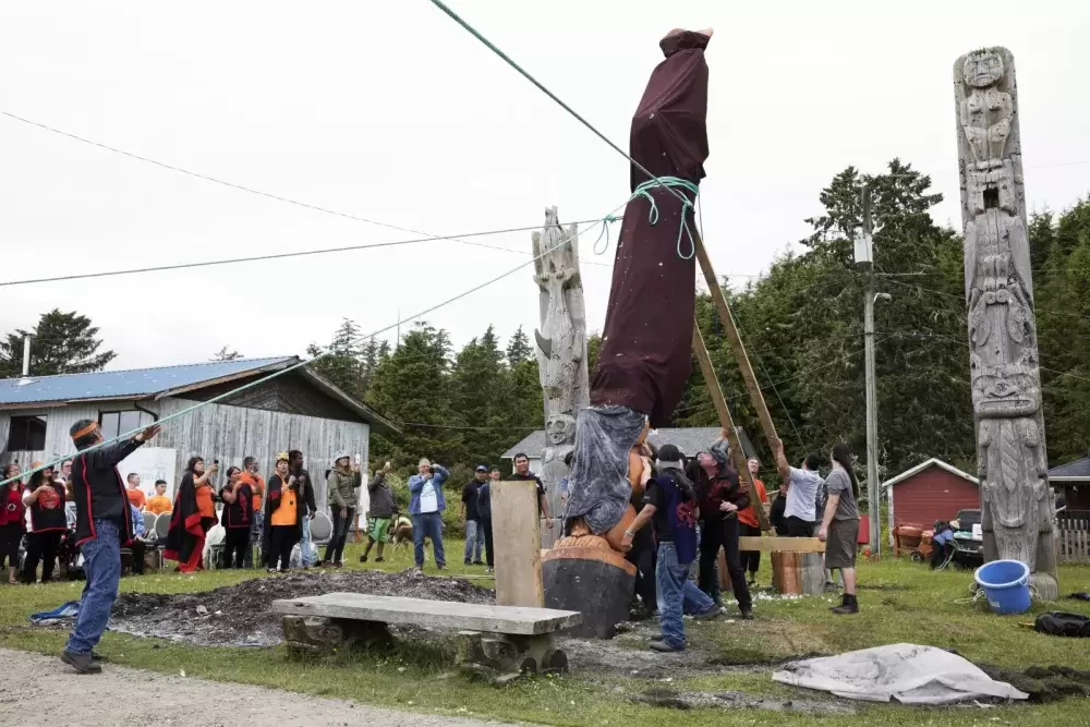 The totem pole is supported by a group of men from behind, as it is pulled up with three ropes, in Opitsaht, on Meares Island, on July 1, 2022.