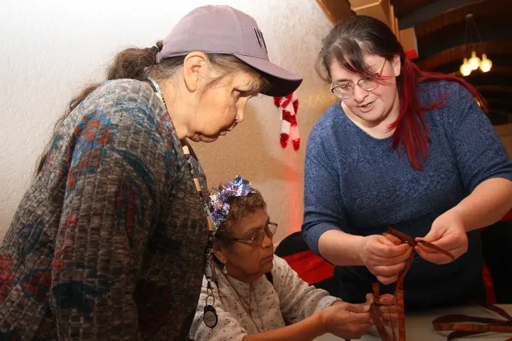 Shirley Galbraith (right) helps Alice George (left) and Cathy Rask with cedar weaving.