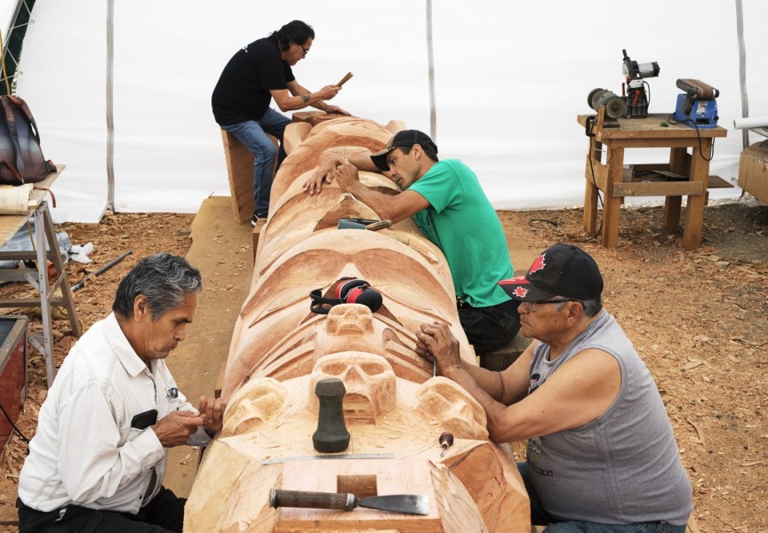 (From left to right) Joe Martin, Patrick Amos, Robin Rorick and Robert Martin (Nookmis) carve a totem pole inside a tent set up at the Tofino Botanical Gardens, on July 9, 2021.