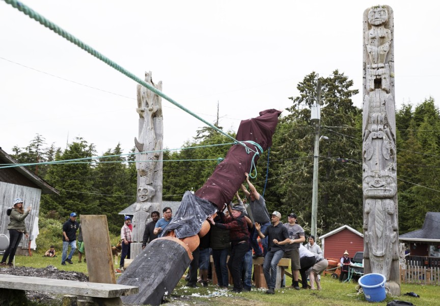 The totem pole is supported by a group of men from behind, as it is pulled up with three ropes, in Opitsaht, on Meares Island, on July 1, 2022.